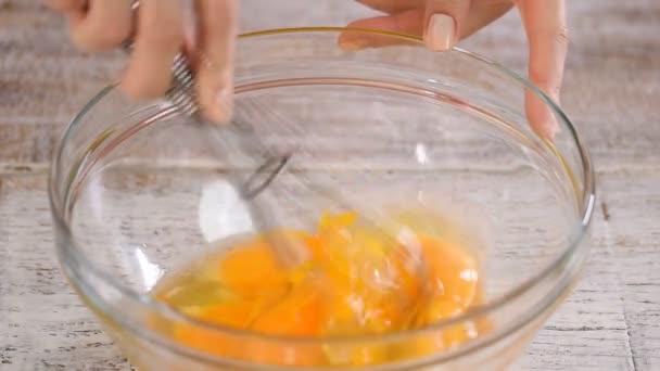 Beating eggs with whisk in glass bowl, on a table. Close-up. - Séquence, vidéo
