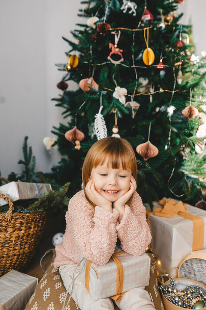 Bambina seduta sul pavimento con i regali sotto l'albero di Natale. Ritratto verticale
 - Foto, immagini