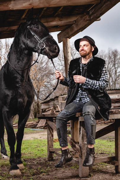 Portrait of a guy in a hat with a black horse. - Fotoğraf, Görsel