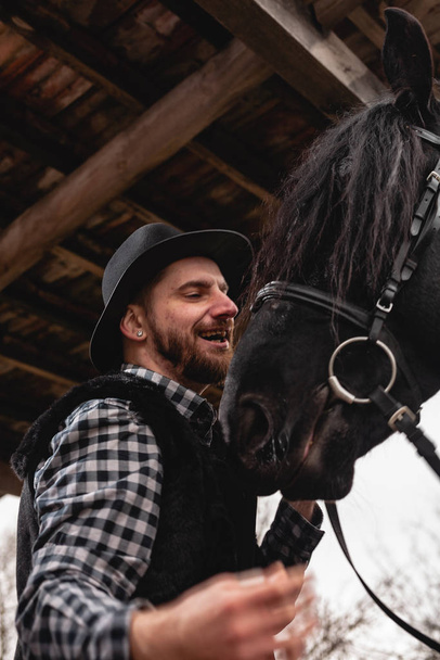 Muotokuva miehestä hatussa mustan hevosen kanssa.
. - Valokuva, kuva