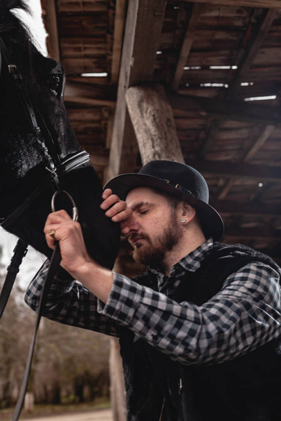Retrato de un tipo con un sombrero y un caballo negro
. - Foto, Imagen