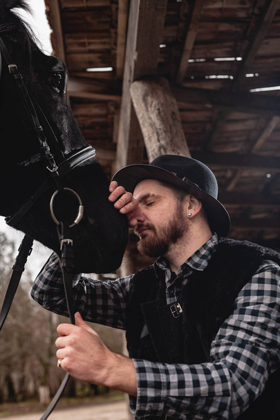 Muotokuva miehestä hatussa mustan hevosen kanssa.
. - Valokuva, kuva