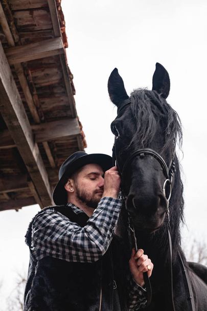 Ritratto di un tizio con un cappello e un cavallo nero
. - Foto, immagini