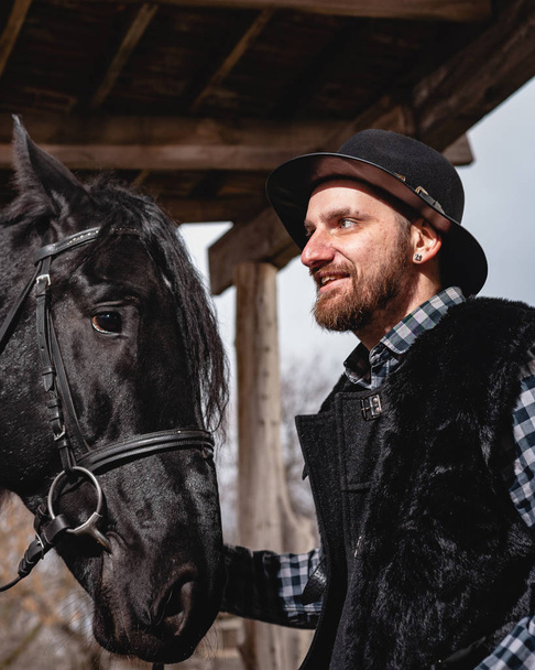 Retrato de un tipo con un sombrero y un caballo negro
. - Foto, imagen