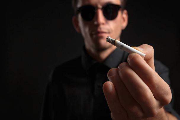 Detailní fotografie stylového mladého muže v černém tričku a slunečních brýlích s cigaretami - Fotografie, Obrázek
