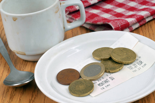 Trinkgeld in einer Untertasse neben einer leeren und schmutzigen Tasse Kaffee - Foto, Bild