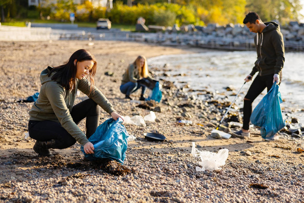 若い女性がビーチで袋にゴミを拾う - 写真・画像