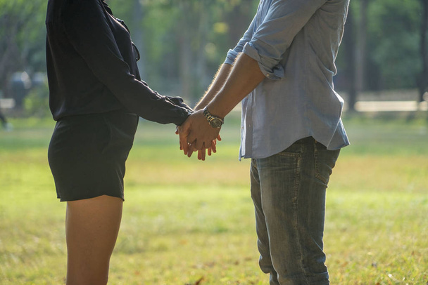  Gelukkig jong stel houdt elkaars hand vast en loopt 's zomers samen in het park. liefde en Valentijnsdag concept. - Foto, afbeelding