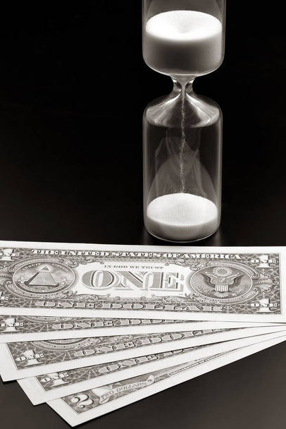 Dollar bills lie near the hourglass. Time is money. The salary.  - Photo, Image