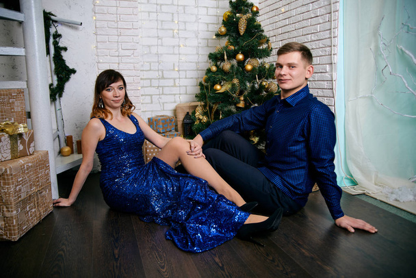 Fiatal, hétköznapi, kétszemélyes család. Fiatal férj és feleség a karácsonyfa mellett. Boldog fiatal hetero pár díszítik karácsonyfa otthon. - Fotó, kép