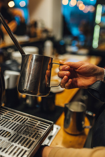 Close up view Barista steaming milk in metal pitcher. Barista making coffee. - 写真・画像