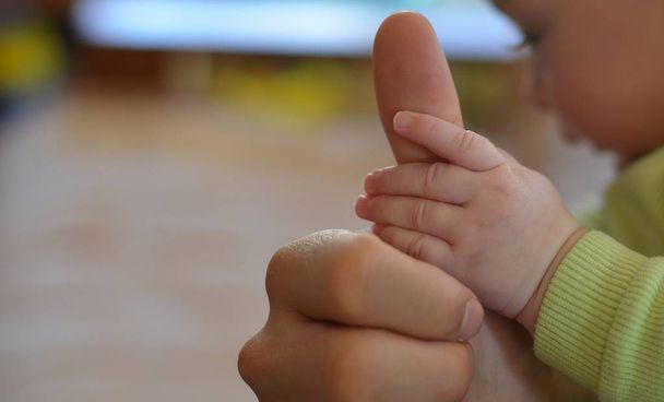 Die Hand des Babys hält den Daumen des Vaters.  - Foto, Bild