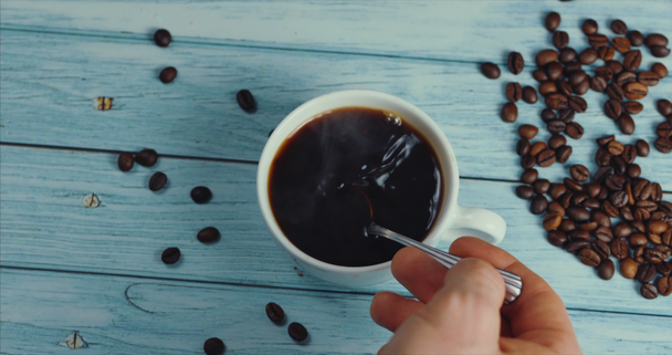 Mannelijke Hand neemt een mok koffie. Koffiekop en koffiebonen. Witte kop stomende koffie op tafel met geroosterde boon. - Video