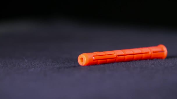 Close-up van oranje plastic deuvel. Voorraadbeelden. Single oranje deuvel ligt op zwarte achtergrond. Dowel wordt gebruikt in de bouw en reparatie met schroeven voor montage in muren - Video