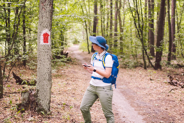 Піші прогулянки позначені стежкою в лісі. Позначення туристичного маршруту, намальованого на дереві. Знак туристичного маршруту. Знак маршруту подорожі. Туристичний пішохід з навігацією рюкзаками використовує смартфон
 - Фото, зображення