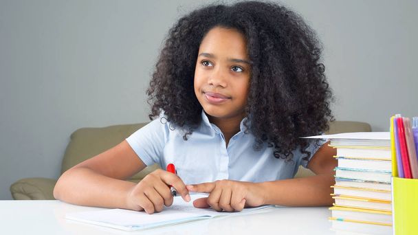 zwarte schoolmeisje schrijft in een notebook, doen huiswerk - Foto, afbeelding