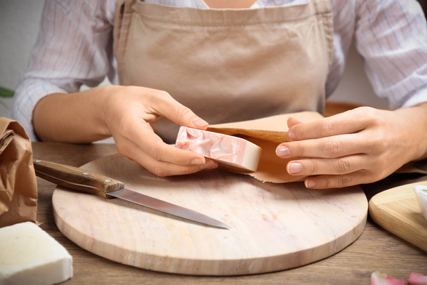 Woman putting natural handmade soap into paper bag at wooden table, closeup - Foto, afbeelding