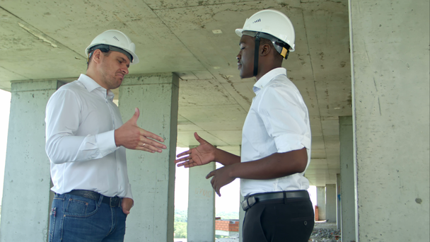 Красивые строительные бизнесмены в защитных шлемах и жилетах пожимают руки на стройке
 - Кадры, видео