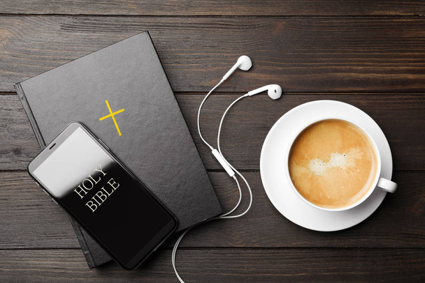 Bible, phone, cup of coffee and earphones on wooden background, flat lay. Religious audiobook - Photo, image