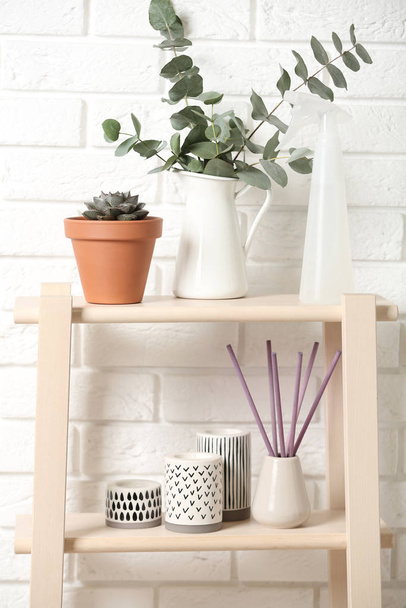 Beautiful plants and accessories on shelves near brick wall at home - Foto, afbeelding