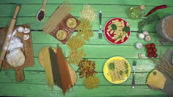 Cooked pasta on plates with spinach. Top View. Green table is divided into many types of dry pasta on the left side and vegetables, cherry tomatoes, cheese, flour and mushrooms on the right side. - Footage, Video