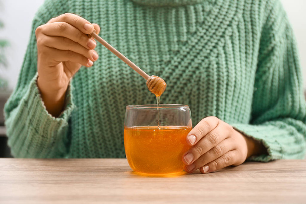 Woman holding honey dipper over jar at wooden table, closeup - Photo, Image