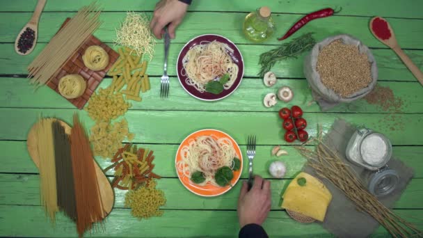 Дегустація спагеті в барвистих тарілках на екологічному столі. Двоє людей їдять спагеті з томатним соусом за вечерею. Смачна традиційна італійська страва. Поруч є олія, овочі, різні види сухих макаронних виробів, гриби
. - Кадри, відео