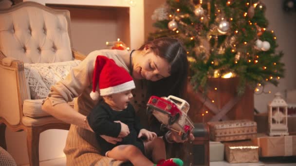 A young smiling woman playing with her little baby with a toy car in christmas studio - Video