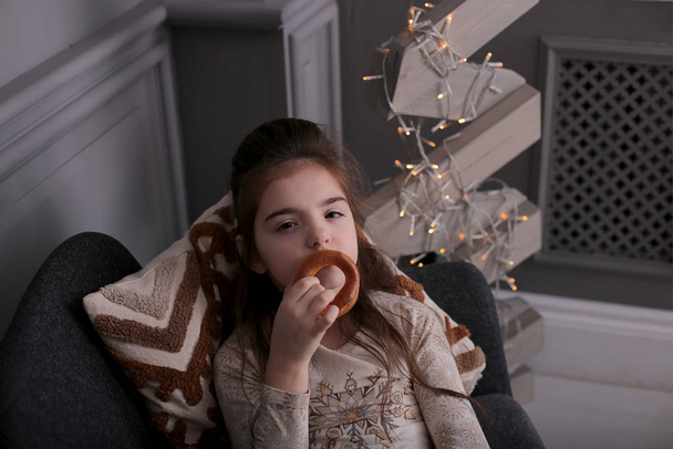 Mooi meisje met lang donker haar rommelt rond met koekjes op Nieuwjaar bokeh lichten op een versierde kerstboom - Foto, afbeelding