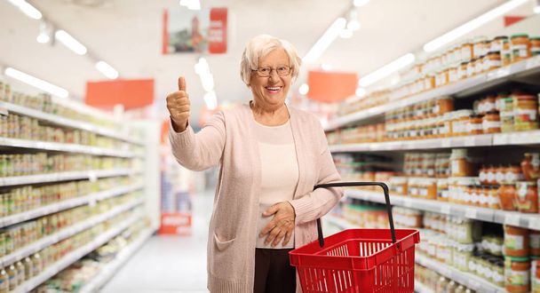 Elderly woman with a shopping basket in a supermarket  - Zdjęcie, obraz