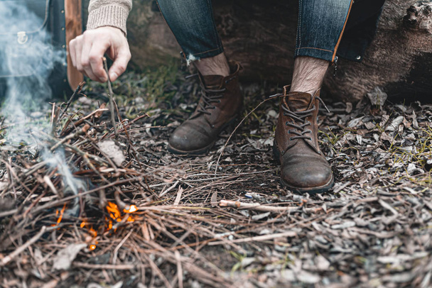 小さな火のそばに座っている自然界の男のストックフォト、自分自身を暖める. - 写真・画像