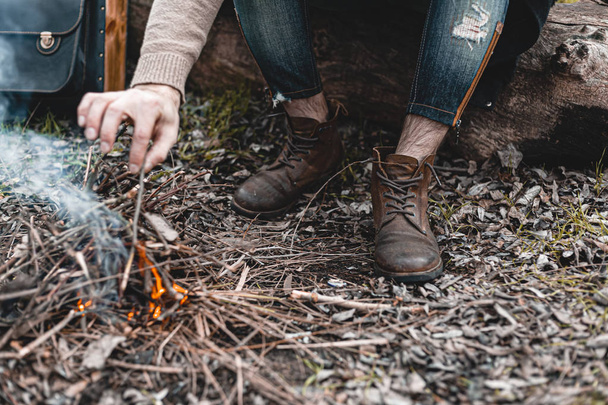 A stock photo of a man in nature sitting by a small fire, warming himself. - Photo, Image