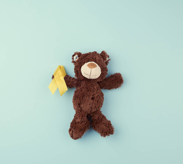 brown teddy bear holds in his paw a yellow ribbon folded in a lo - Photo, Image