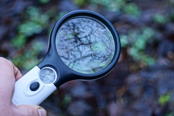 hand holds a big black white plastic magnifier outdoors - Photo, image