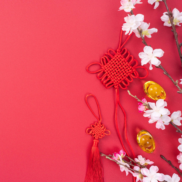 Design concept of Chinese lunar new year - Beautiful Chinese knot with plum blossom isolated on red background, flat lay, top view, overhead layout. - Photo, image