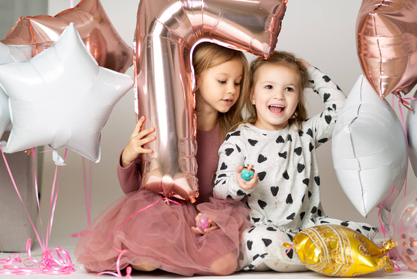 Gelukkige verjaardag 7 jaar. kleine meisjes in avondjurk kijken uit een ballon in de vorm van een zeven op witte achtergrond met kralen - Foto, afbeelding