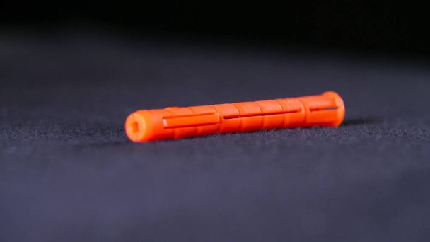 Detailní záběr oranžového plastového hmoždíře. Záběry ze skladu. Jeden oranžový kolík leží na černém pozadí. Hmoždinka se používá při stavebních a opravných pracích se šrouby pro montáž do stěn - Fotografie, Obrázek
