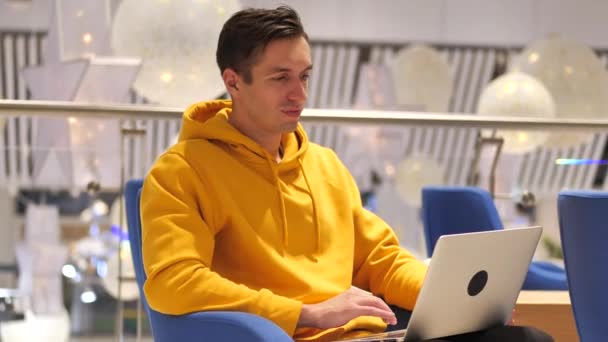 νεαρός άνδρας που εργάζεται σε φορητό υπολογιστή σε ένα μεγάλο σύγχρονο καφέ  - Πλάνα, βίντεο