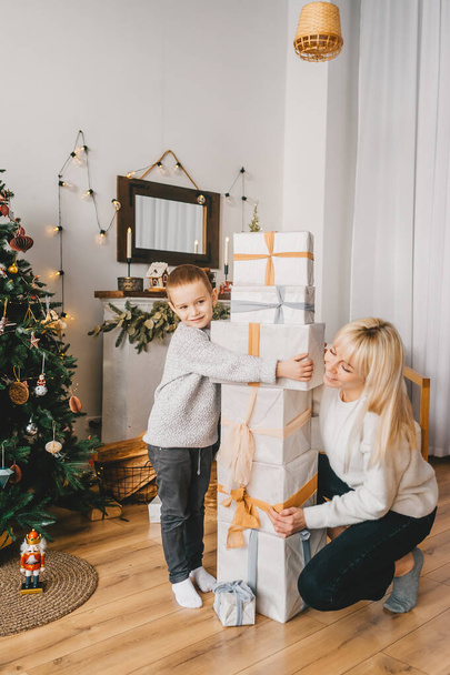 Счастливая мать и ее маленький сын. Перед семьей, есть много красиво упакованные коробки с подарками
.  - Фото, изображение