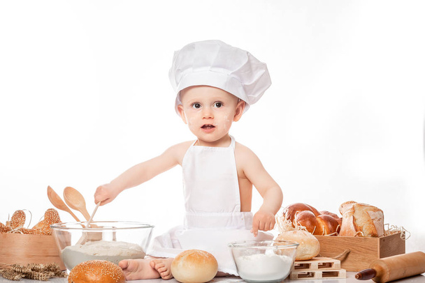 bebé cocinero se sienta en la harina de pan de mesa pan. Pequeño bebé chef con pan - Foto, imagen