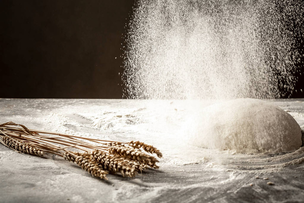 Chef in a kitchen sprinkles flour on the table to make dough. Empty space for text. Isolated on dark background - Photo, Image