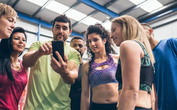 Αθλητές που κοιτάζουν το κινητό ενός συμπαίκτη τους στο γυμναστήριο - Φωτογραφία, εικόνα