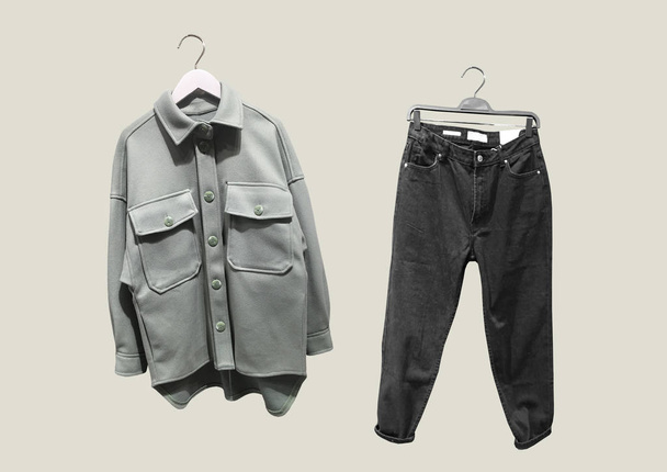 ポケット付きブラックジーンズとグレーの背景に隔離されたハンガーにポケット付きグリーン合成ウールオーバーシャツのコラージュ。服の構成。流行の服のコラージュ。パターン - 写真・画像