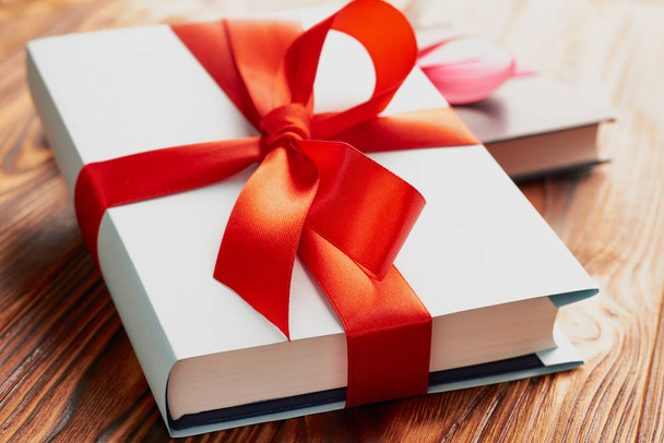 Close-up of a book tied with a ribbon with a bow on a lying on another book: the concept of a good book - a good gift - Фото, изображение