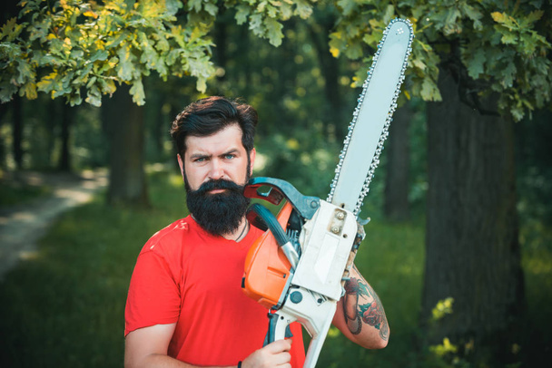 Woodcutter with axe or chainsaw in the summer forest. Lumberjack with chainsaw in his hands. - Valokuva, kuva