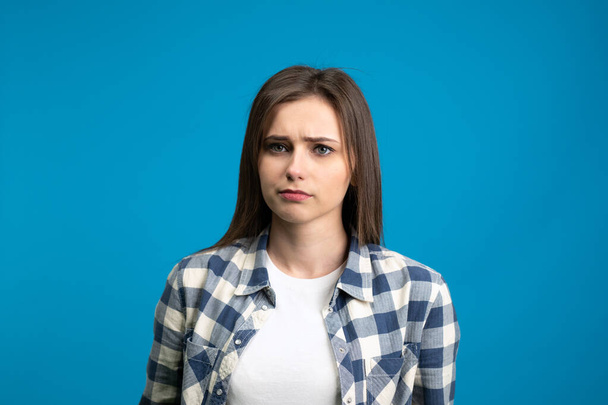 Front view of sad young woman looking at camera isolated on blue background - Photo, Image