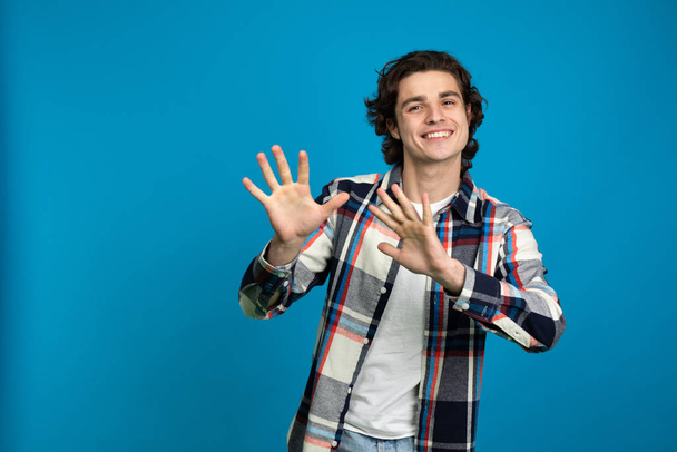 Nadšený mladý muž v kostkované košili gestikulace izolované na modrém pozadí - Fotografie, Obrázek
