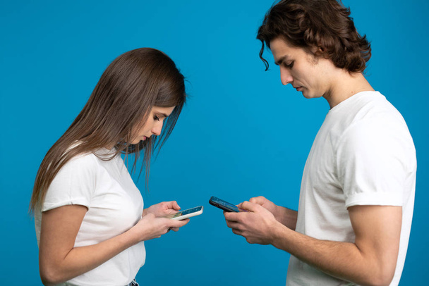 Вид сбоку молодой женщины и мужчины, использующих смартфоны, изолированные на синем фоне
 - Фото, изображение