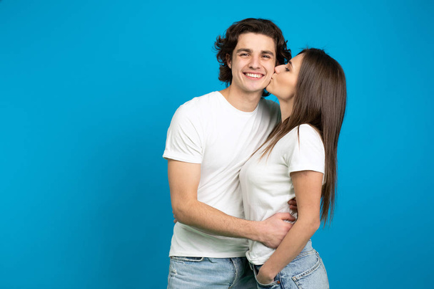Pretty girl kissing boyfriend isolated on blue background - Foto, imagen
