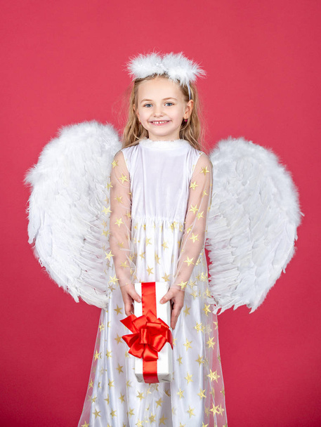 Angel child from heaven gives you gift. Cute toddler girl in white wings as Cupid. Angel kid with blonde curly hair. Happy little Angel. Wonderful blonde little girl in the image of an angel with - Фото, изображение
